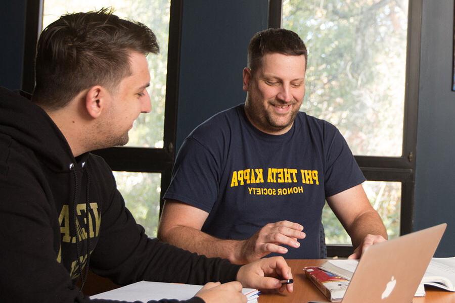 两个男学生坐在会议桌旁. 一名学生的运动衫上写着Phi Theta Kappa荣誉协会.